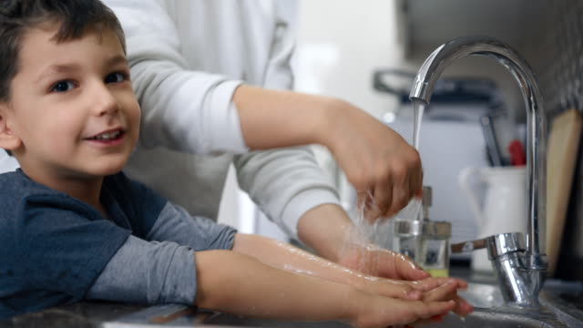 Mother And Son Wahing Hands Together in Kitchen