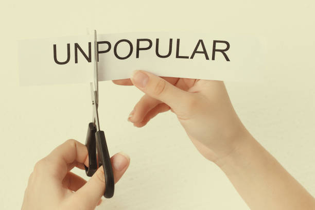 istock Female hands scissor the word unpopular 1214646930