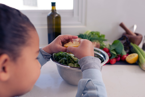 Close up over shoulder view of 6 years old girl seasoning, squeezing a lemon into the salad.
