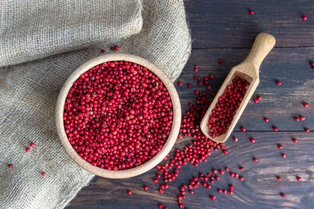 pimienta roja o rosa ("pimienta de brasil" o "schinus terebinthifolius") en cuenco de madera y cuchara de cerca en la mesa oscura rústica - pink pepper fotografías e imágenes de stock