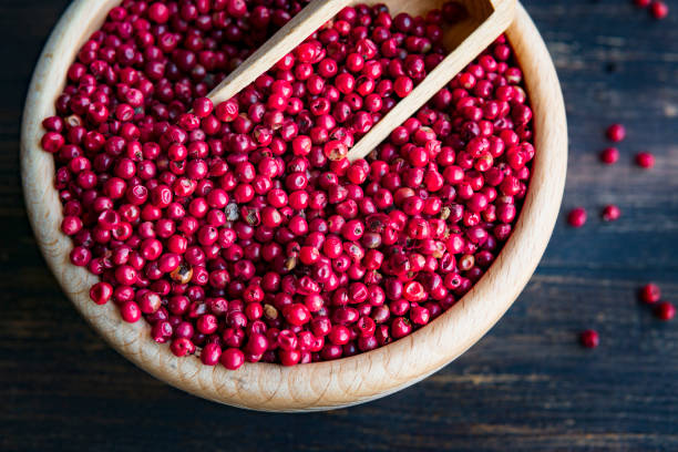 rote oder rosa pfefferkörner ("brasilien pfeffer" oder "schinus terebinthifolius" ) in holzschale und löffel nah auf rustikalen dunklen tisch - pink pepper fotos stock-fotos und bilder