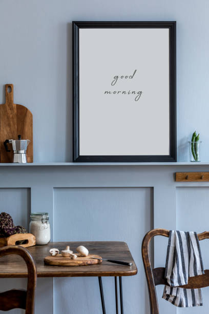 istock Interior design of kitchen space with black mock up photo frame, wooden table, chairs, herbs, cutting board, food and kitchen accessories in modern home decor. 1214651117