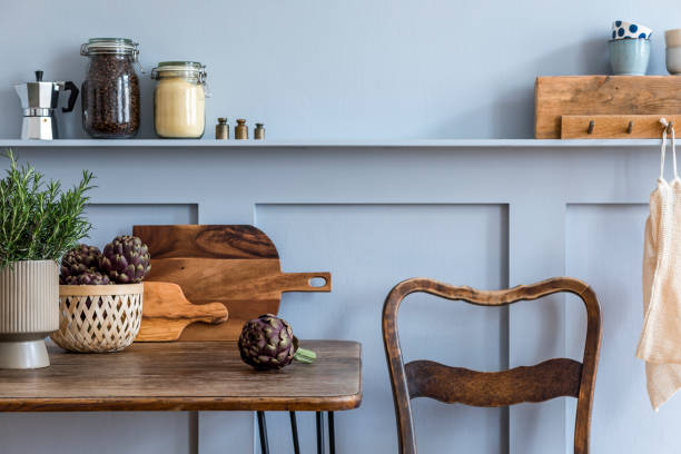 Stylish composition of kitchen interior with wooden family table, vegetables, herbs, plants, food supplies and kitchen accessories in gray concept of home decor.