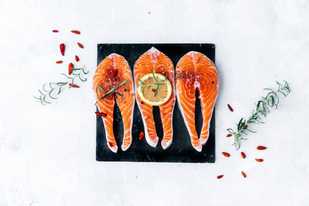сырой лосось с травами и лимонами на фоне шифера - freshness seafood crushed ice salmon стоковые фото и изображения
