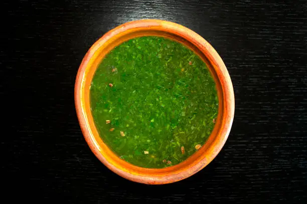 Photo of Molokhia soup in brown bowl on dark wooden background.