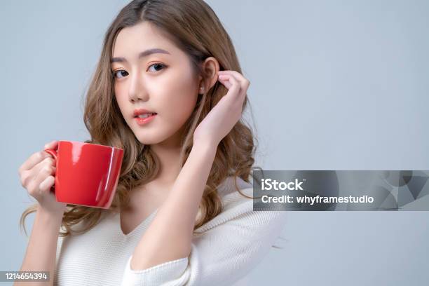 魅力的なアジアの美しい女性の女性の手は、カメラの肖像画スタジオでホットカップコーヒードリンクの外観を持って白い背景を撮影