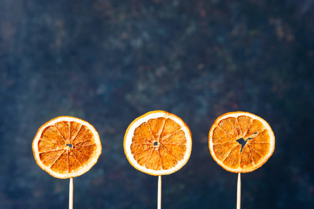 istock Three dried orange slices on wooden sticks, dark background. 1214656518