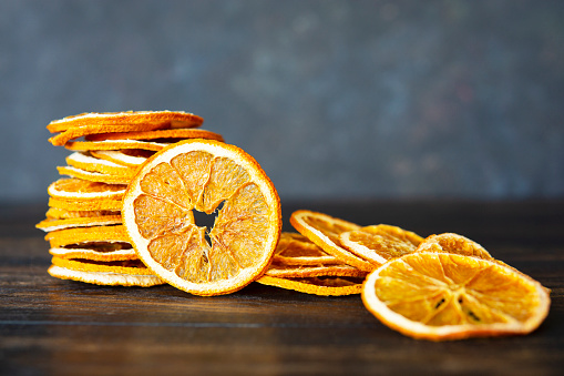 Dried orange slices on brown wooden table, dark background. Natural light. Organic fruit product. Copy space.