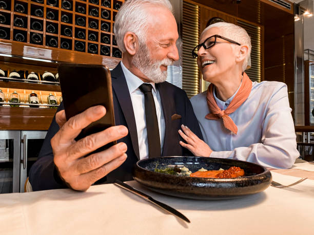 istock Senior elegant man using a mobile phone while having dinner with his partner in an exclusive restaurant 1214658589