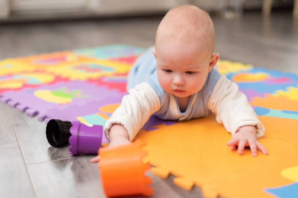 maluch bawi się na podłodze. niemowlę leży na brzuchu na dywanie z piramidą. - one baby boy only zdjęcia i obrazy z banku zdjęć