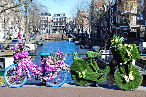 Front view of two bikes adorned with flowers and grass by one the main water canals in the center of Amsterdam.