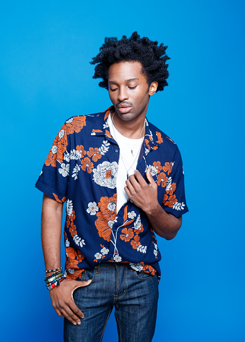 Fashion portrait of afro american young man with dreadlocks wearing hawaiian short sleeved shirt. Studio shot on blue background.
