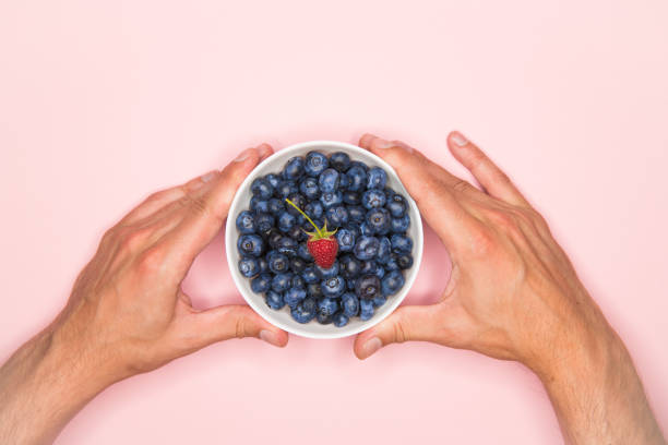 Woman holding a handful of fresh blueberries and strawberries. Horizontal framing, shallow depth of field used.