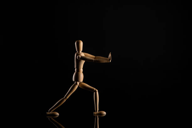 Wooden doll imitating doing lunges on black background
