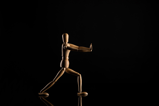 Wooden doll imitating doing lunges on black background
