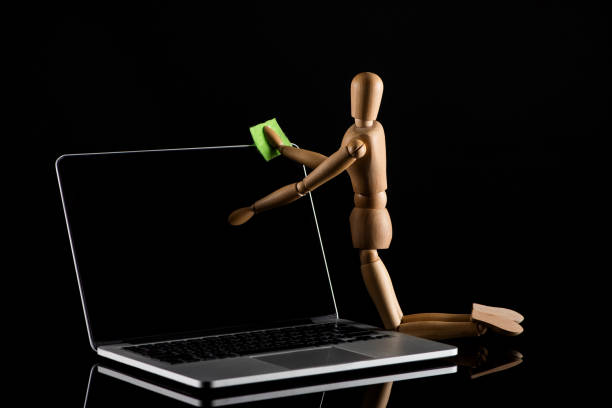 istock Wooden doll on knees position imitating dusting laptop on black 1214671378