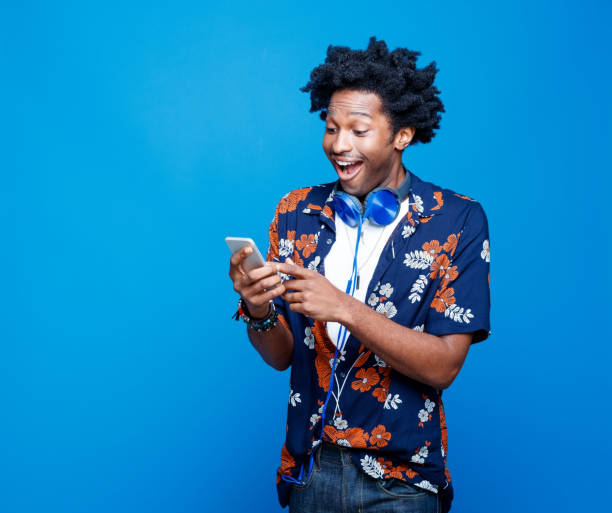 スマートフォンを持つハワイのシャツを着た驚いた若者 - floral pattern audio ストックフォトと画像