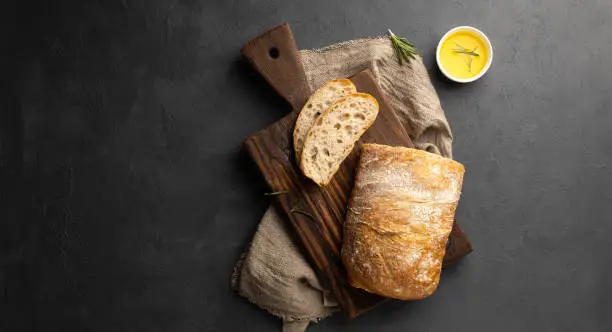 Crispy Italian ciabatta bread on black background. Top view, flat lay.