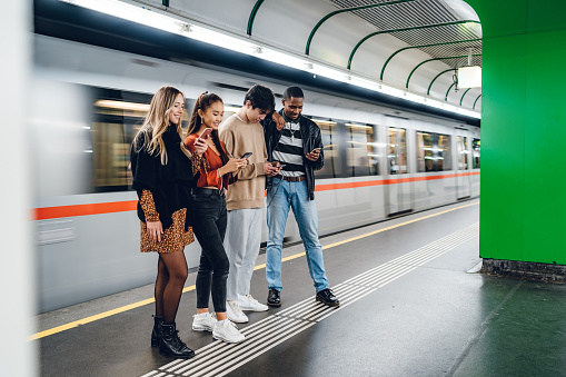 Group of multi-ethnic teenagers using phones in subway station. Social issues concept.