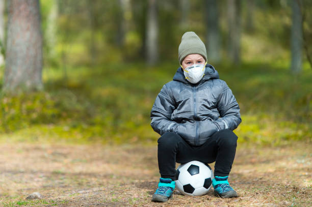 Little boy with a mask and soccer ball in the park. Corona virus quarantine Little boy with a mask and soccer ball in the park. Corona virus quarantine face guard sport photos stock pictures, royalty-free photos & images