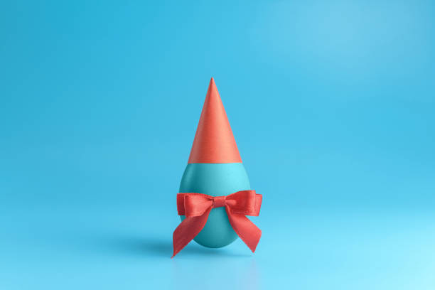 istock One blue egg with a red ribbon bow in a red festive cap on a blue background. 1214688601