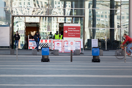 Frankfurt, Germany - March 25, 2020: Main entrance of Universitaetsklinikum (University hospital) Frankfurt and waiting visitors. In the foreground numerous boards and signs with safety instructions because of corona pandemic