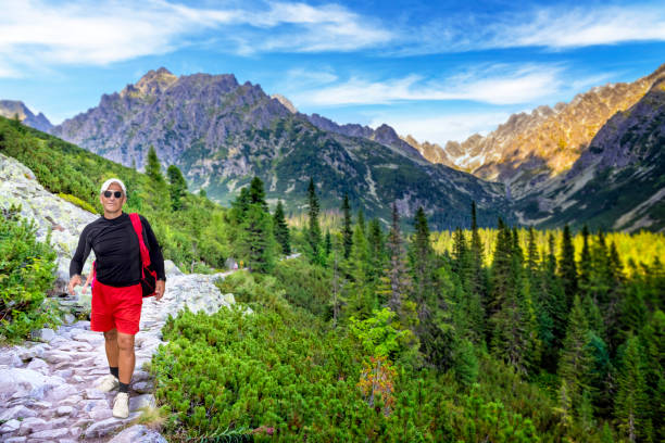 Middle-aged tourist goes along the Tatra Mountain path over the Mieguszowiecka valley towards the Strbske Pleso in Tatra Mountains, Slovakia