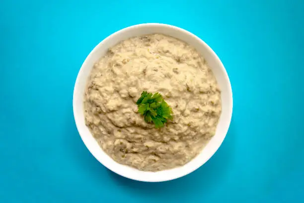 Photo of dip Baba ghanoush in whire bowl with fresh green parsley on blue background