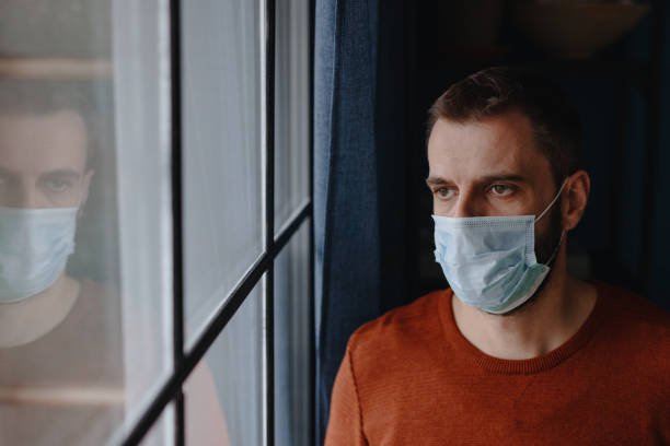 istock Man wearing protective face mask and looking trough window 1214692285