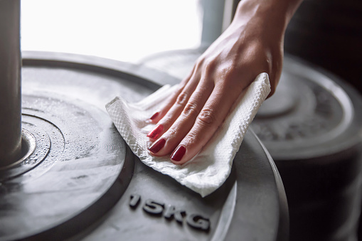 Close up shot female hands wiping weight plates surface , before and after workout to keep hygiene and avoid virus