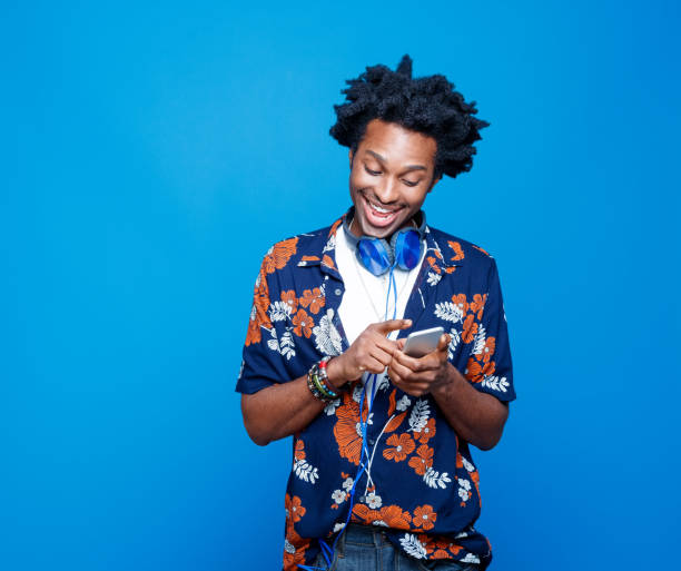 homem satisfeito com camisa havaiana usando telefone inteligente - men smiling headphones individuality - fotografias e filmes do acervo