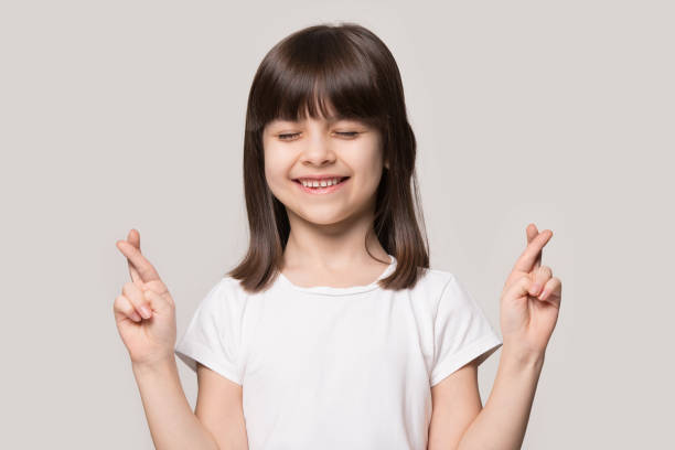 istock Smiling small girl cross fingers making wish 1214694474