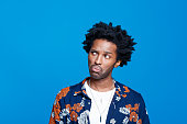 Worried young man in hawaiian shirt against blue background