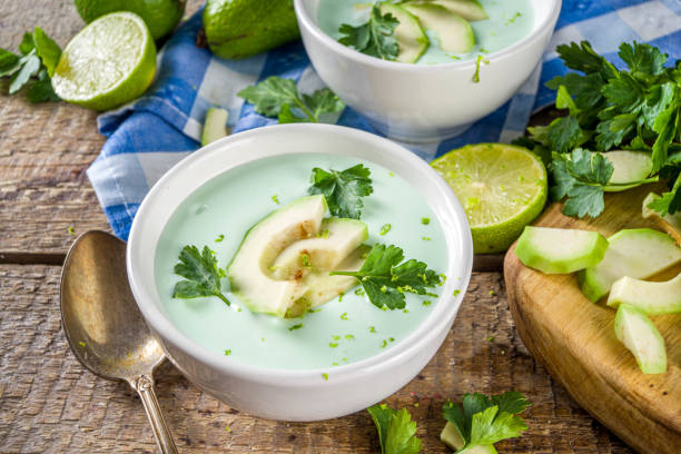 Homemade avocado cream soup with lime, herbs and avocado slices on wooden rustic background, copy space