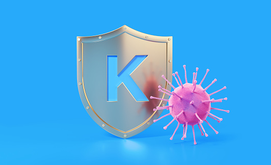 K vitamin written gold colored shield protecting from a virus on blue background, Horizontal composition with copy space. Health concept.