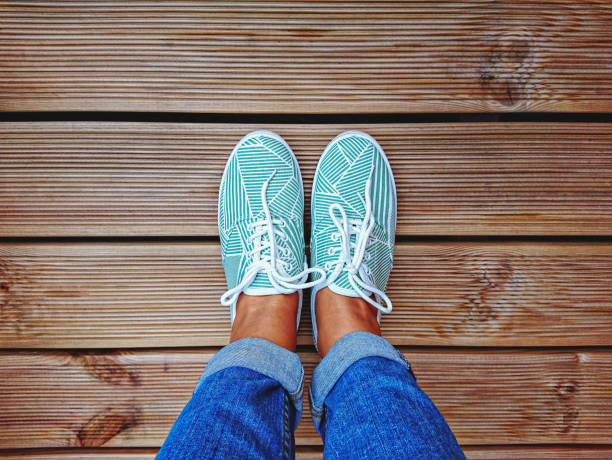 Women's legs in mint green sneakers on terrace board with copy space. Women's legs in mint green sneakers on terrace board with copy space. Top view and personal point of view personal perspective standing stock pictures, royalty-free photos & images
