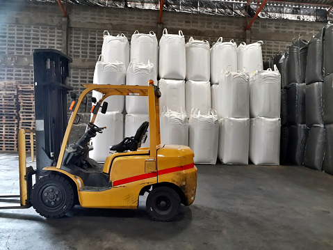 Big yellow car loader and White hemp sacks containing chemical fertilizer in the warehouse.