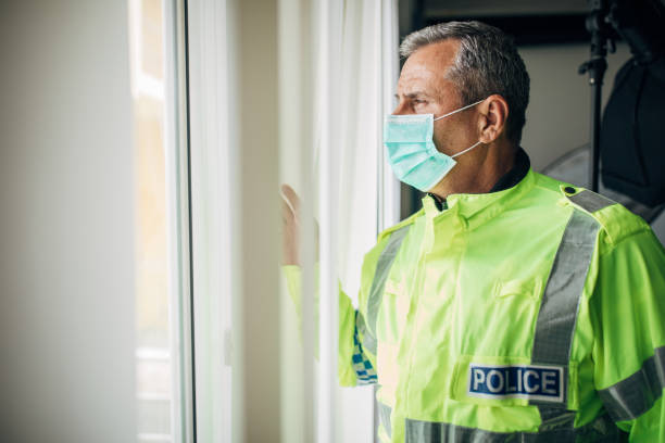 Senior police officer with protective mask Senior British police officer with protective mask looking through the window from the office. Fight against coronavirus. civil servant stock pictures, royalty-free photos & images