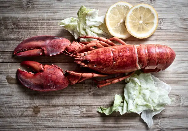 Photo of Red lobster with vegetable and lemon on wooden cutting board background , top view / Lobster dinner