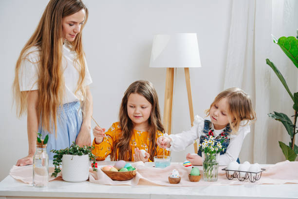 istock Young mother watching her two daughters painting easter eggs behind a table 1214715798