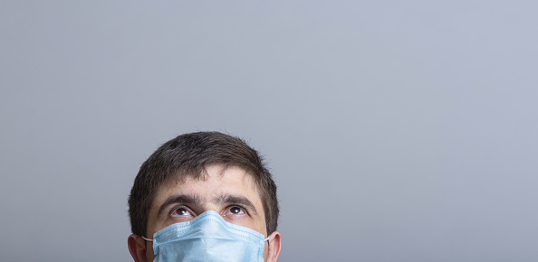 head of a young man in protective surgical mask looking up and following news, concept of health and medicine, place for advertising clinic services