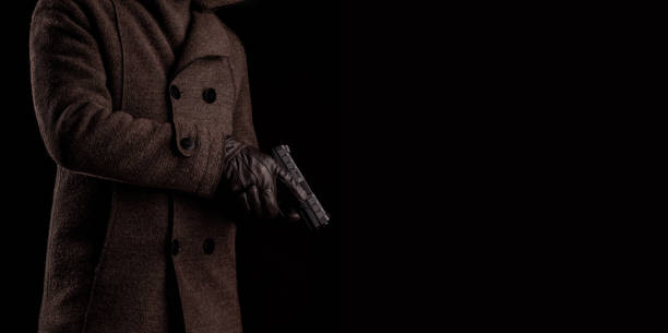 a man in a dark coat holds a gun. security guard or bodyguard with arms in hand. black pistol in the hands of a man. - gun men spy suit imagens e fotografias de stock