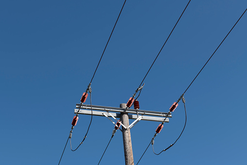 A utility pole (column or post) made of timber (wood) supporting overhead power lines on the Greek Island of Chios on a sunny midday with clear blue sky in spring.