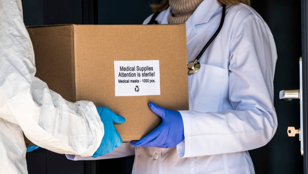 A person in a protective suit is handed a box with protective medical masks to the doctor stock photo