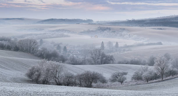 istock Panoramic Rural Landscape With Wavy Plowed Fields, Trees In Hoarfrost And Old Windmill In Morning Fog. Winter Arable Land. Beautiful Frosted Cultivated Field. Frozen Grass. Christams In Moravia, Czech Republic 1214723255