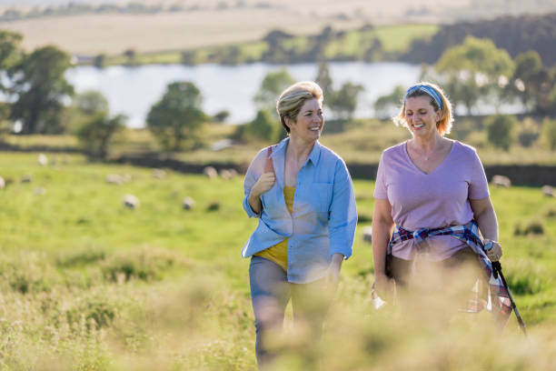 It's Good to Talk Mature Caucasian female friends enjoying walking in the countryside on a sunny day with a stunning view behind them. nordic walking pole stock pictures, royalty-free photos & images