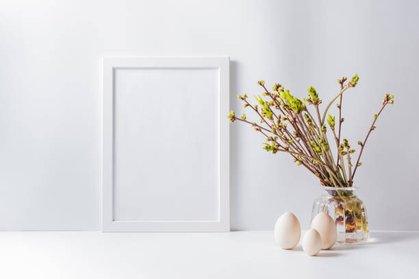 istock Home interior with easter decor. Mockup with a white frame and green buds on branches in a vase on a light background 1214726936