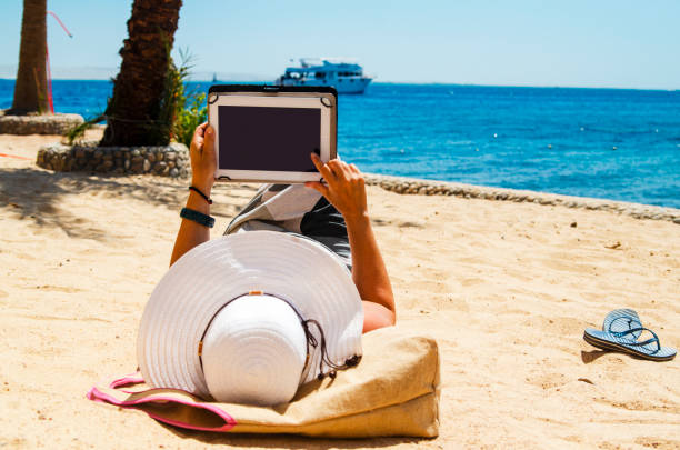 istock Reading favorite e-book on the beach 1214727315
