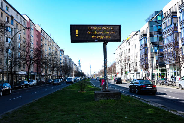 Berlin traffic billboard with health advice during coronavirus shutdown in Germany Berlin, Germany - March 24, 2020: Road sign reminding commuters of restrictions and social distancing by avoiding unnecessary movement and contacts during coronavirus shutdown in Germany. friedrichshain photos stock pictures, royalty-free photos & images