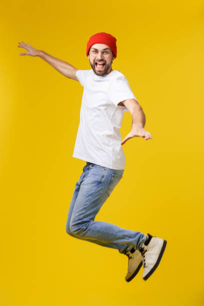 istock young casual man jumping for joy on yellow gold background 1214730208